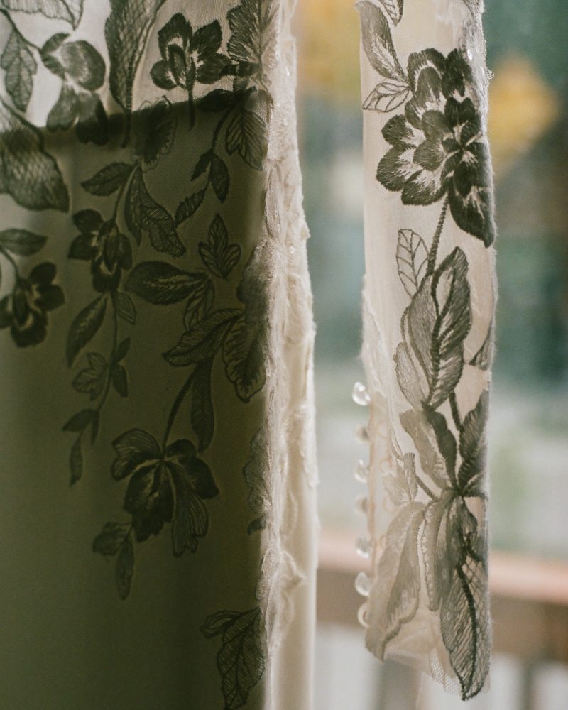 Close-up of sheer white fabric with intricate floral embroidery, frayed edges, and small buttons, perfect for a Calgary elopement or wedding. The soft natural light and blurred background create a calm and delicate atmosphere.