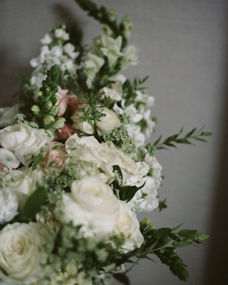 A bouquet of white and pale pink flowers, including roses and greenery, arranged against a neutral gray background—perfect for a Calgary wedding or intimate elopement.