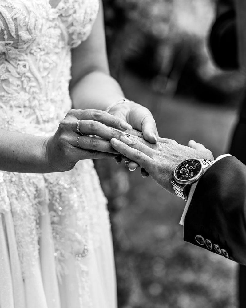 A bride in a lace wedding dress places a ring on her partner’s finger during an intimate elopement ceremony. Captured by a Calgary photographer, this black and white image highlights their hands at the unforgettable moment.