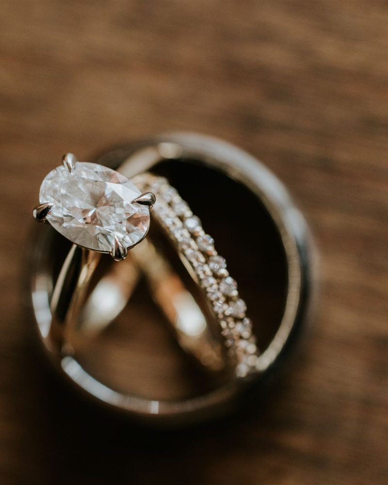 Close-up of three rings on a wooden surface: a diamond engagement ring, a diamond-studded wedding band, and a plain metal band, arranged together in a circle—perfect for any Banff wedding photographer to capture.