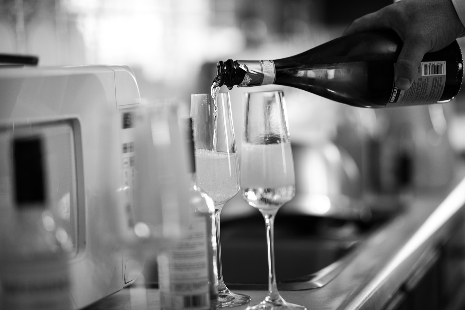 A photographer captures a hand pouring sparkling wine into tall, narrow glasses on a counter at a Calgary wedding, with bubbles forming in the glasses. The elegant black and white image exudes timeless celebration.