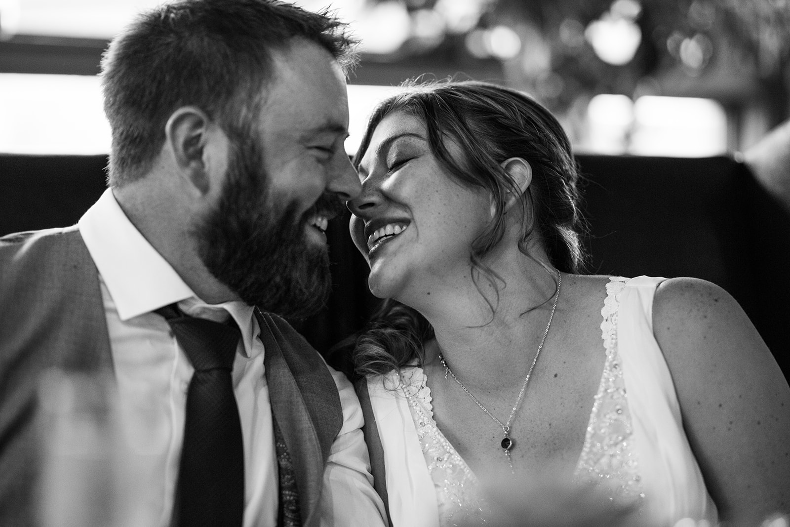 A joyful bride and groom sit closely together, smiling and touching noses, sharing an intimate, happy moment on their Canmore elopement. The photo is black and white.