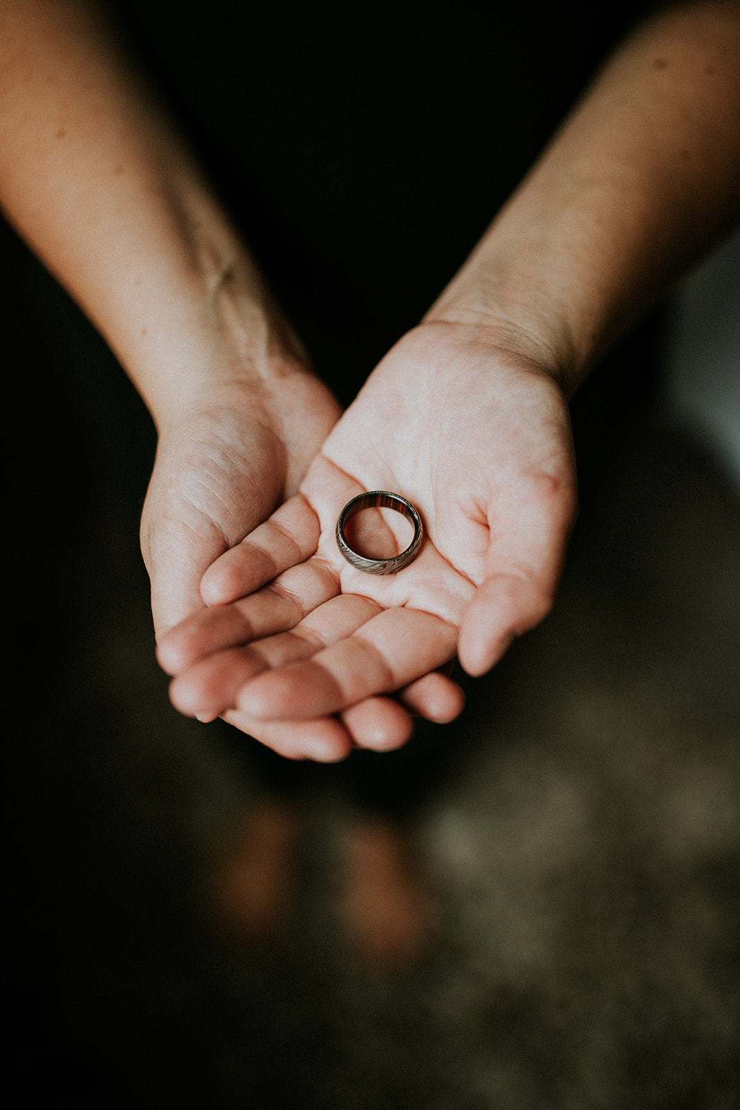 A person holds out their open hands, palms up, with a silver ring resting in the center. Captured by a Calgary photographer, the softly blurred background adds a dreamy touch.