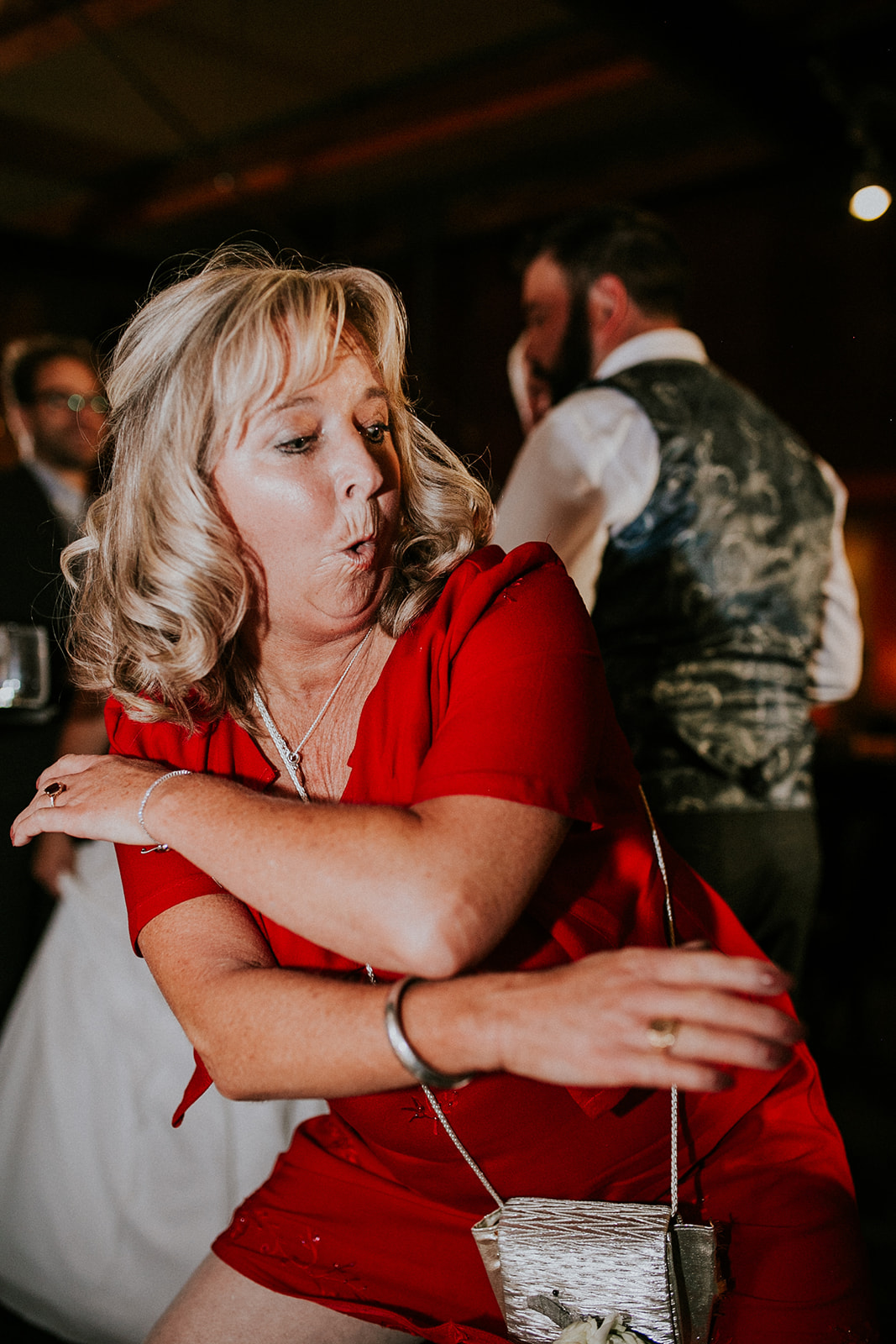 A woman with blond hair in a red dress energetically dances at a party, making a playful facial expression. Captured by a Calgary photographer, people in formal attire are visible in the blurred background.