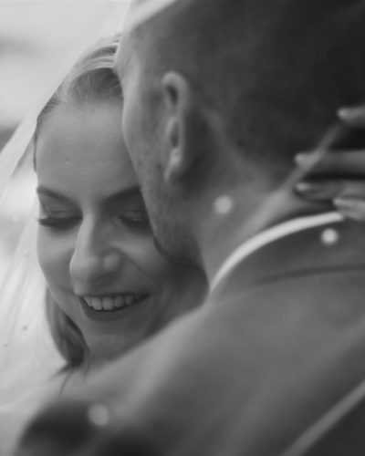 A black and white close-up of a bride smiling with her eyes closed while a groom gently embraces her, his face turned away. Capturing an intimate Calgary wedding elopement, the bride’s ringed hand rests on his neck as her veil softly drapes around them.